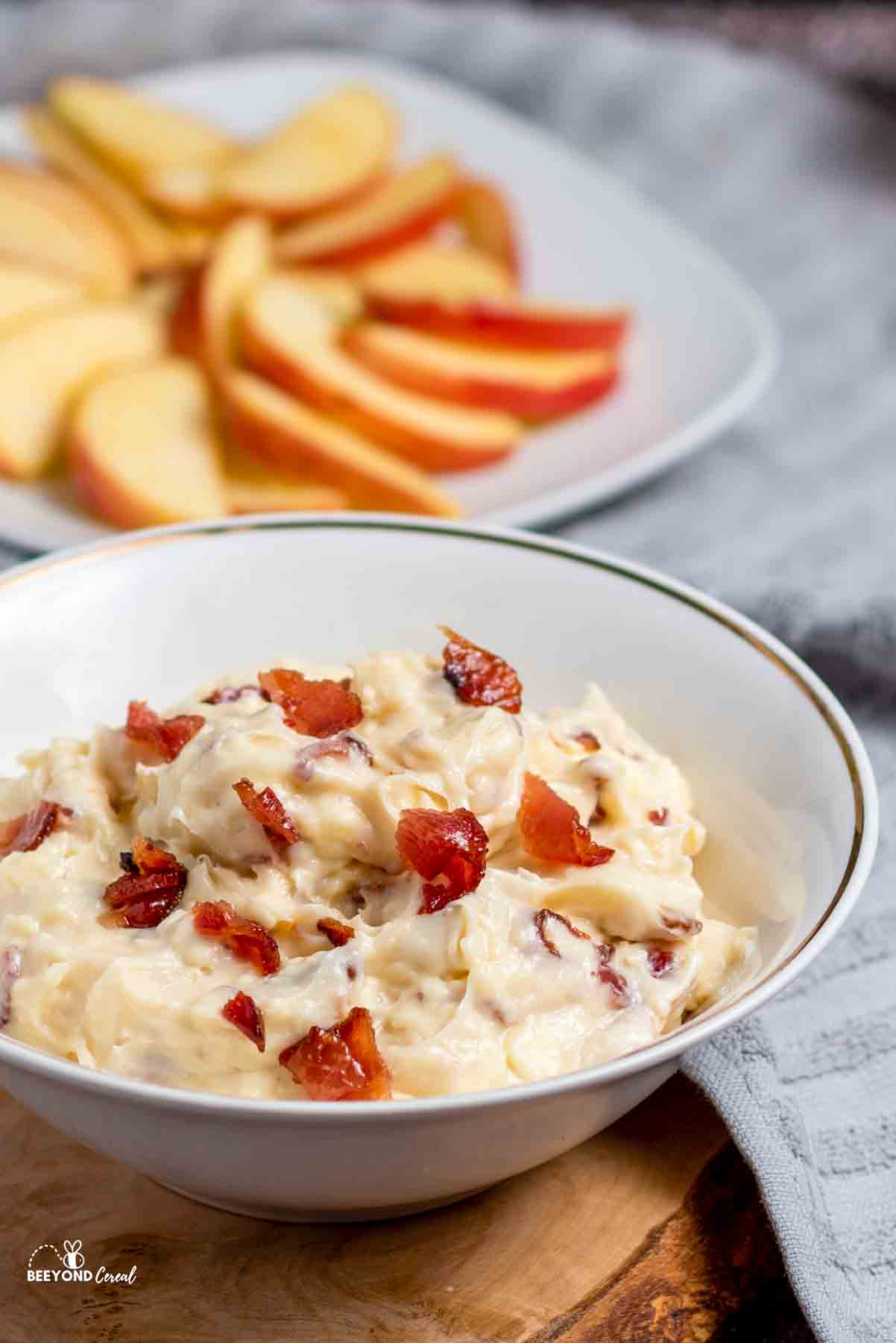 maple bacon dip in a bowl topped with cooked bacon and a plate.