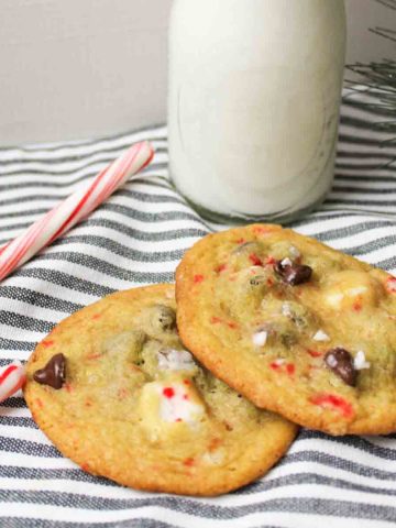 two chocolate chip peppermint cookies next to a candy cane.