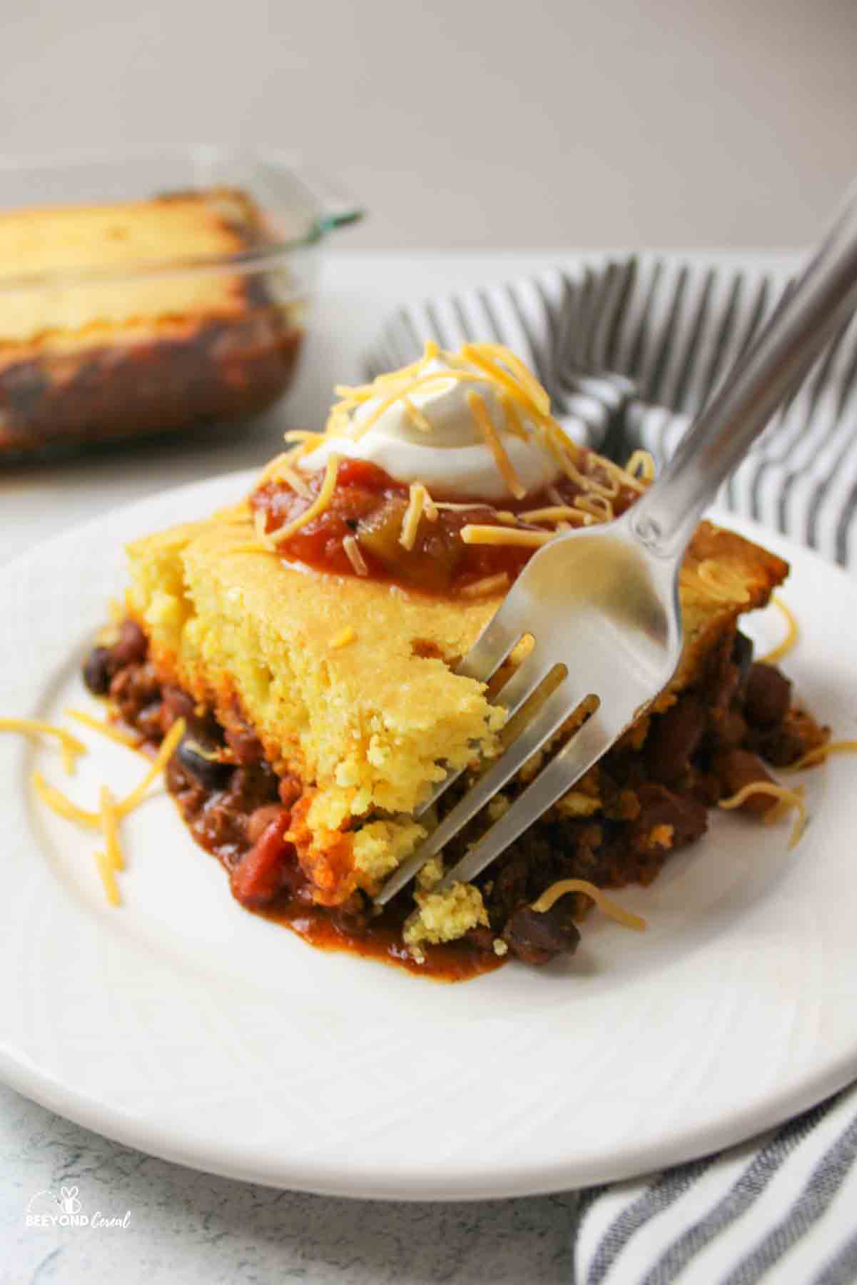 a fork scooping out a bite of tamale pie from a serving on a plate