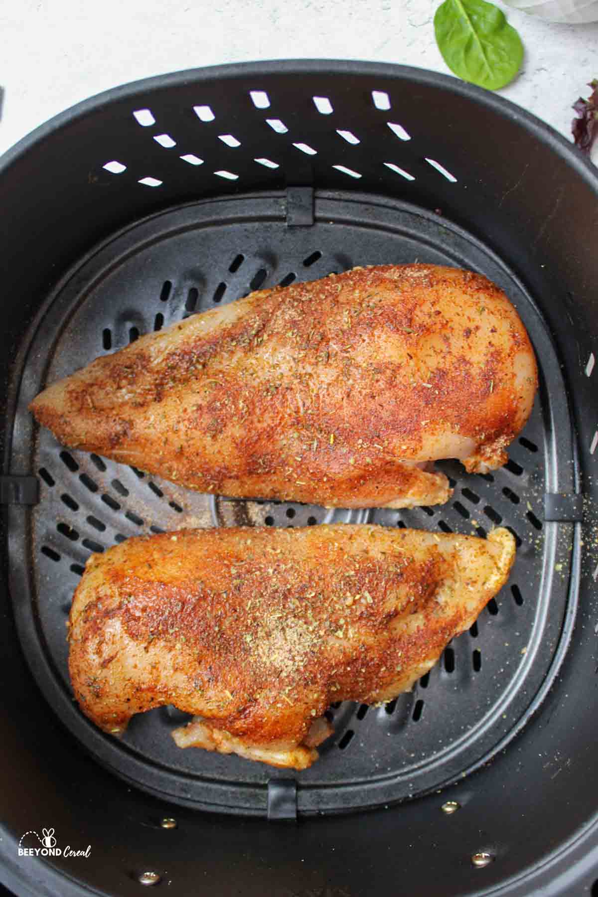 two seasoned raw chicken breasts in an air fryer.