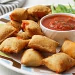 a plate full of air fried pizza rolls next to a bowl of marinara sauce.