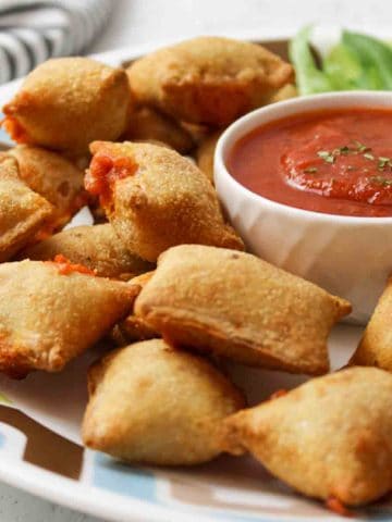 a plate full of air fried pizza rolls next to a bowl of marinara sauce