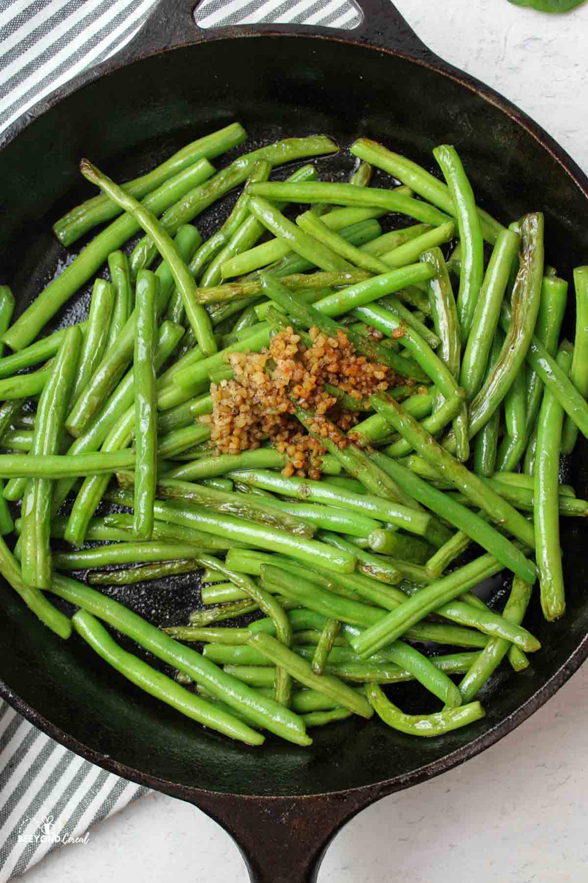 aerial view of sauteed green beans in skillet with garlic and seasonings added on top