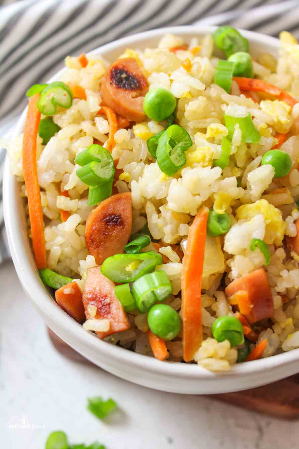 a bowl filled with hot dog fried rice and garnished with sliced green onions.