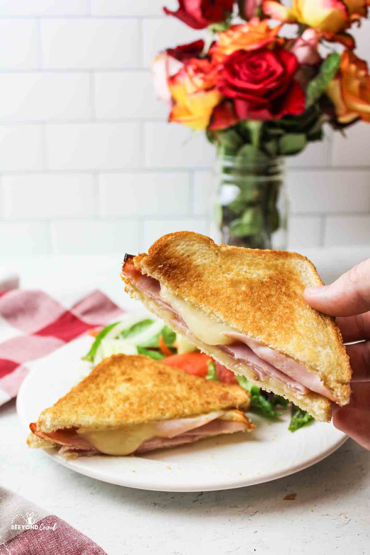 a hand holding up half of an air fried grilled ham and cheese sandwich.