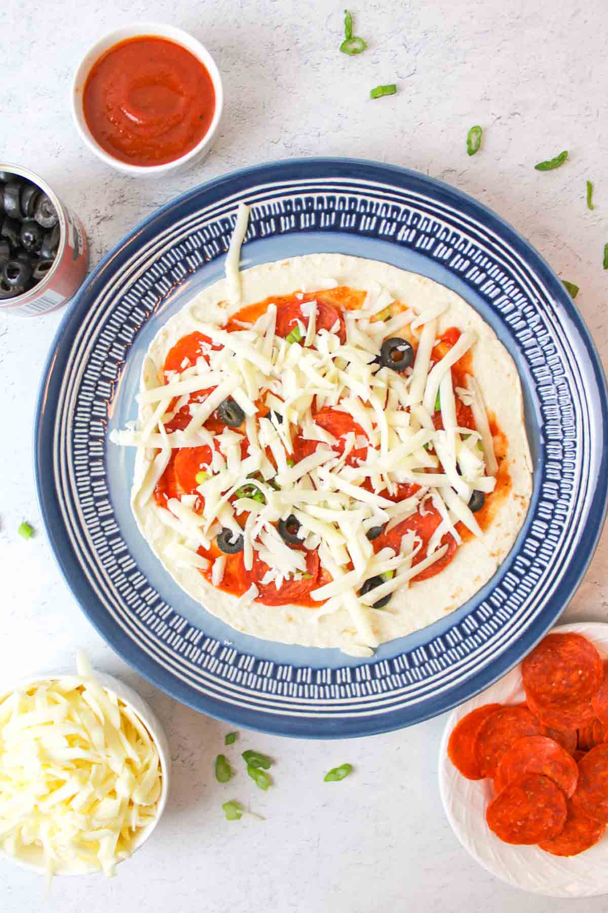 a tortilla pizza with sauce and toppings under shredded cheese on a blue plate