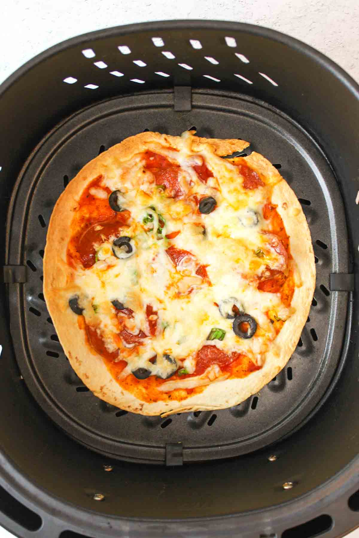 cooked air fryer tortilla pizza in a air fryer basket