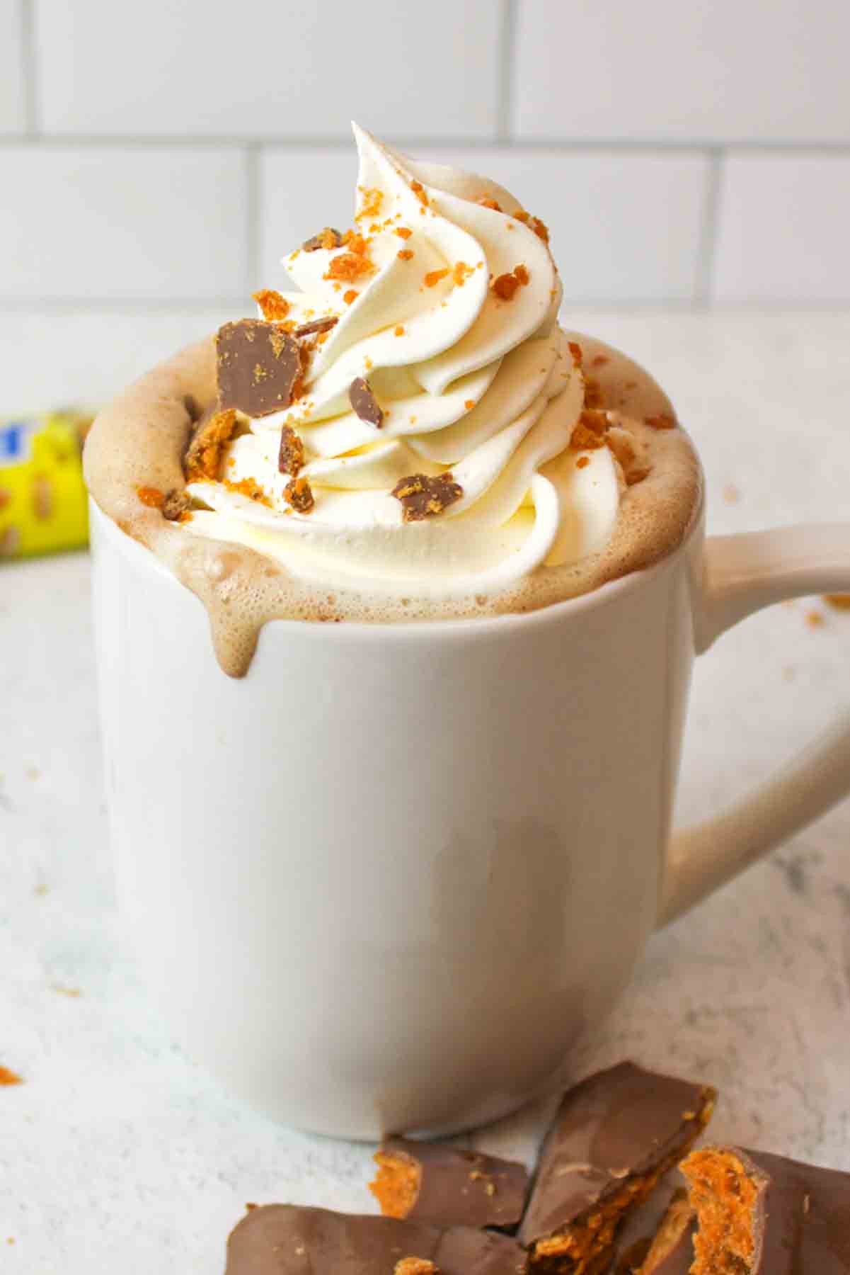 a mug filled with butterfingers hot chocolate and topped with whipped cream and crushed butterfingers candy.