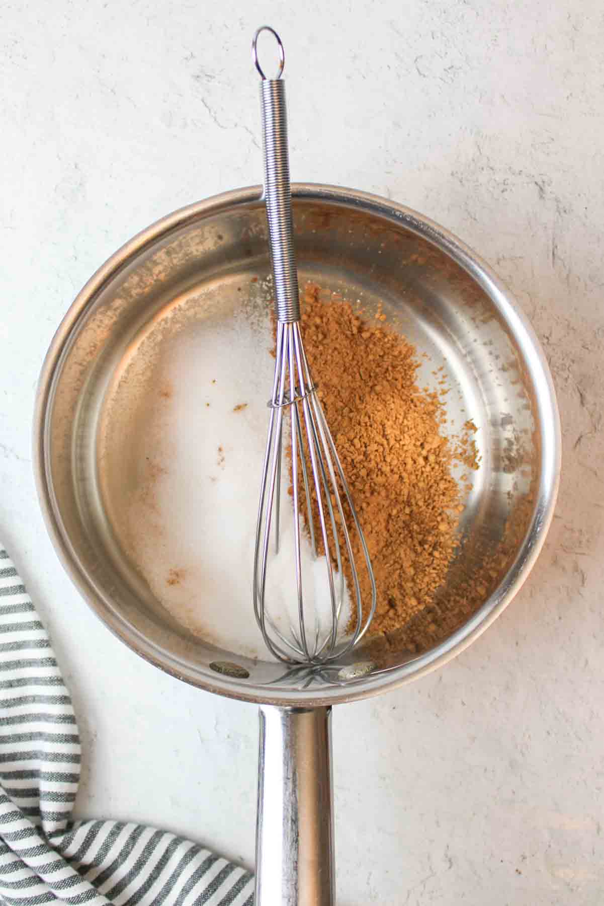 a metal pot with a whisk, sugar, and cocoa powder inside