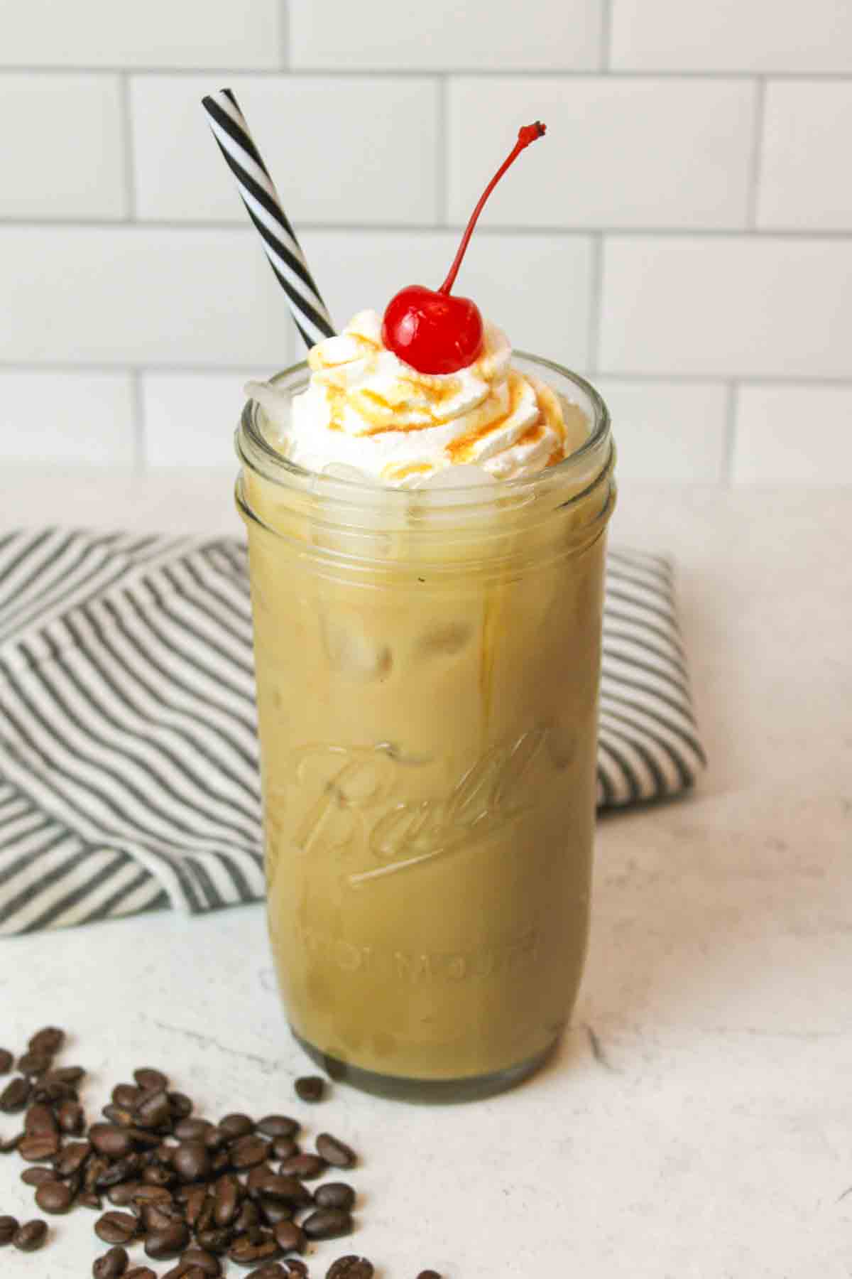 a tall mason jar glass filled with Caramel Iced Coffee and some scattered coffee beans to the side
