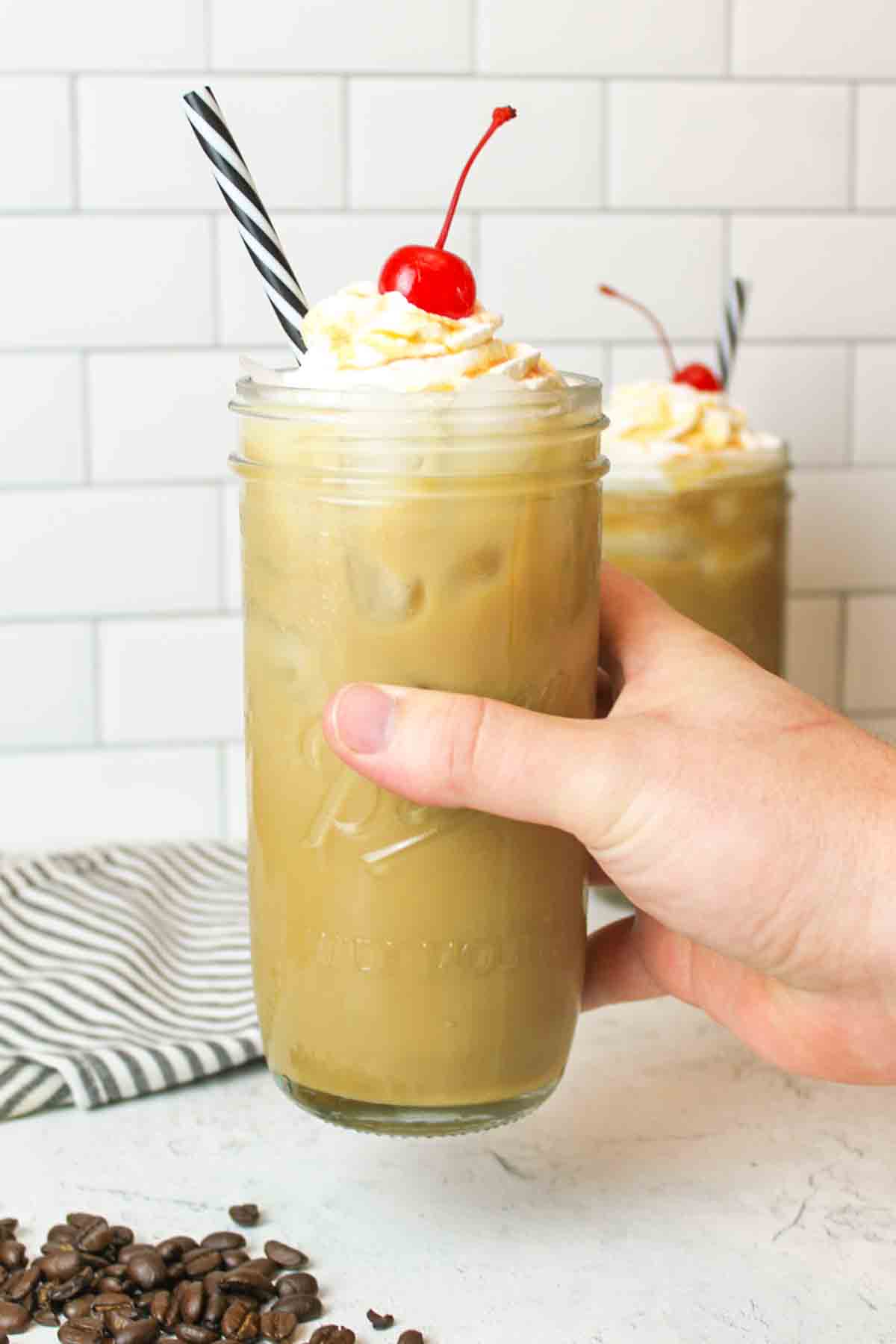 a hand grabbing a tall glass of Caramel Iced Coffee