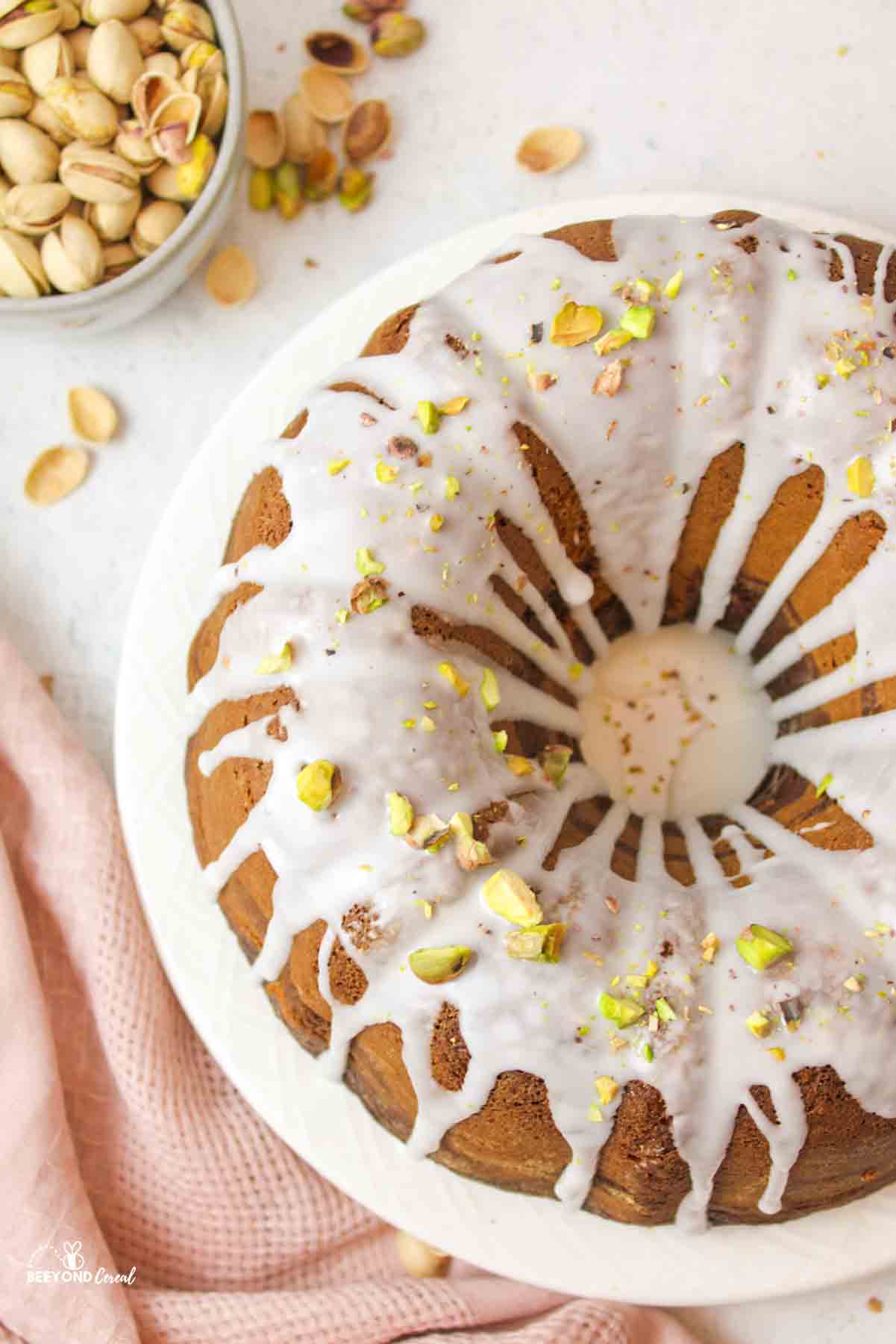 aerial view of a glazed and garnished Chocolate Pistachio Bundt Cake with pistachios off to the side