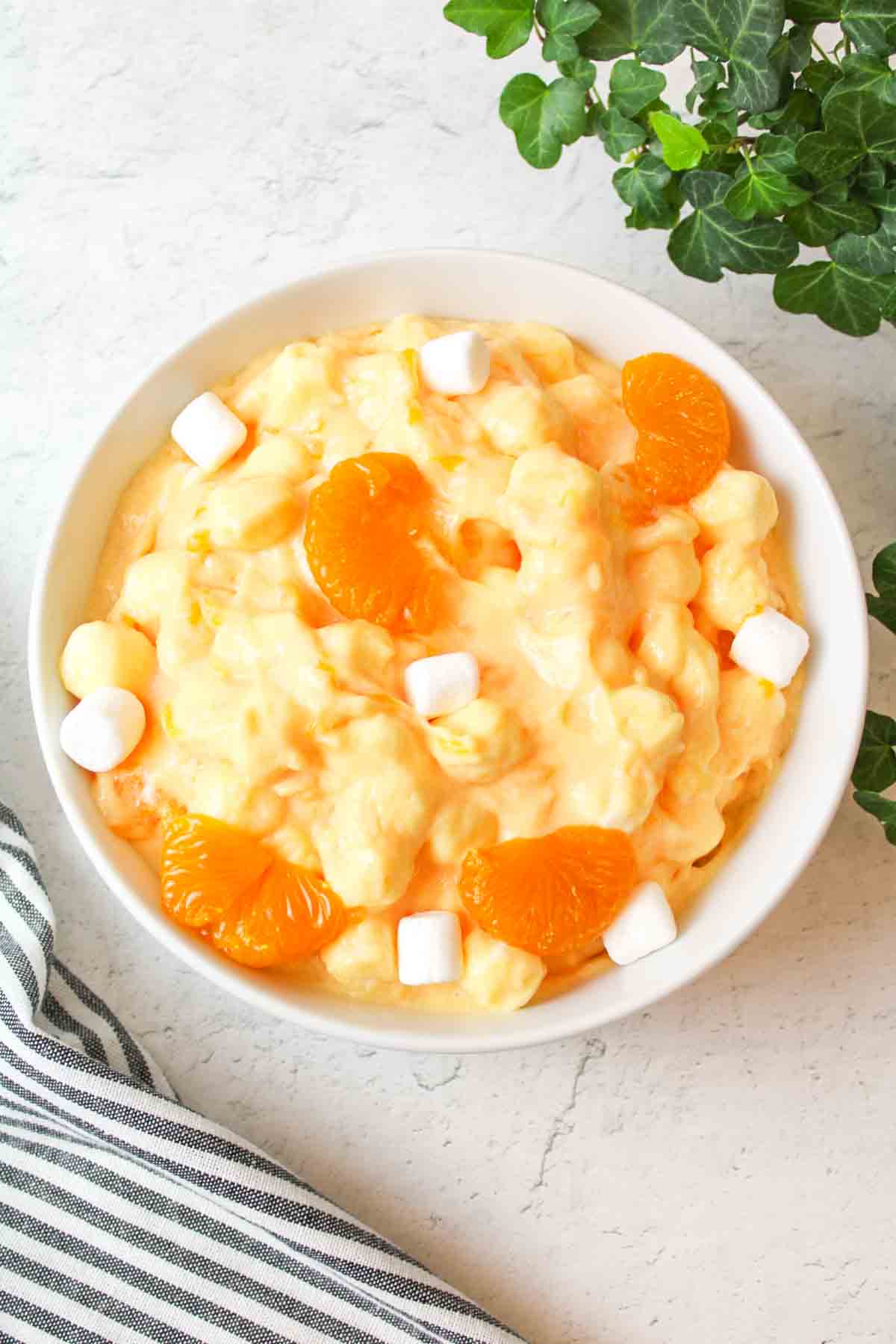 aerial view of orange fluff salad in a white bowl with marshmallows and orange slices