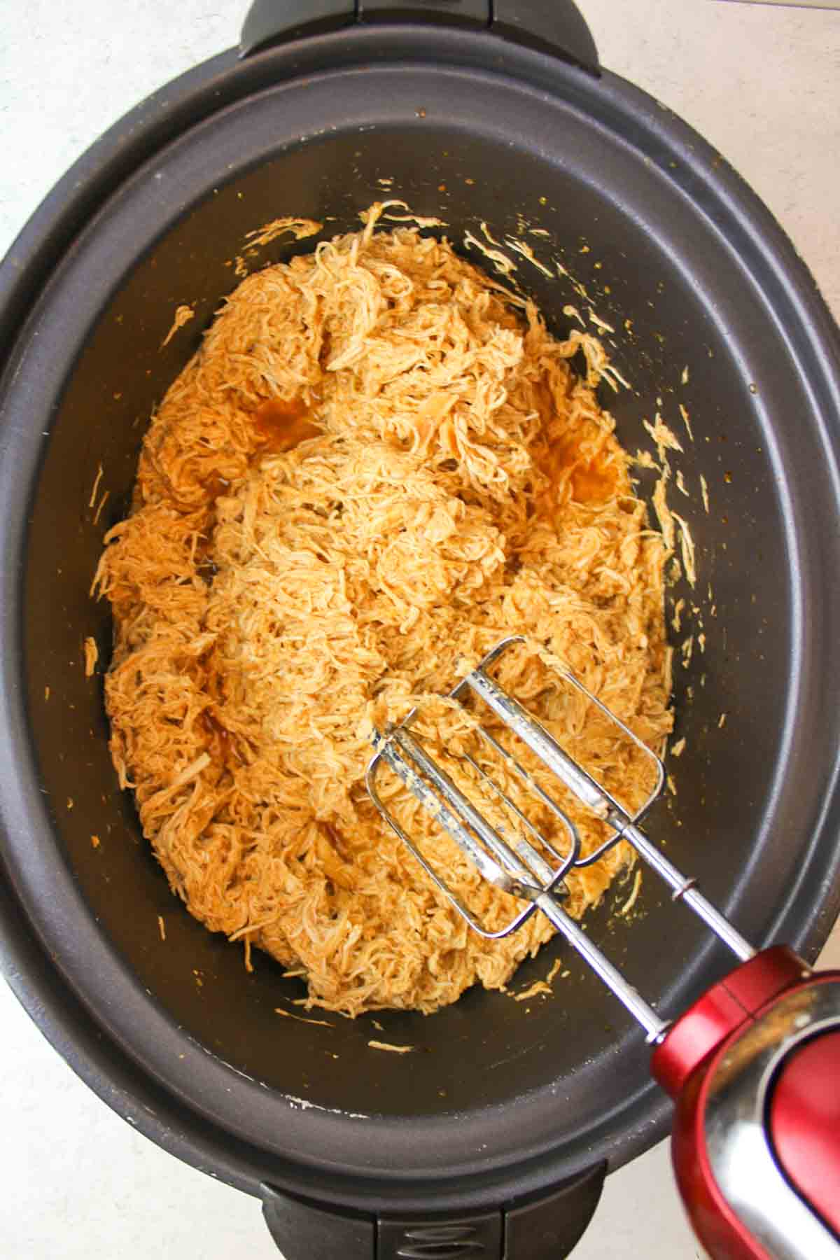 cooked enchilada chicken shredded in a crockpot with an electric mixer.