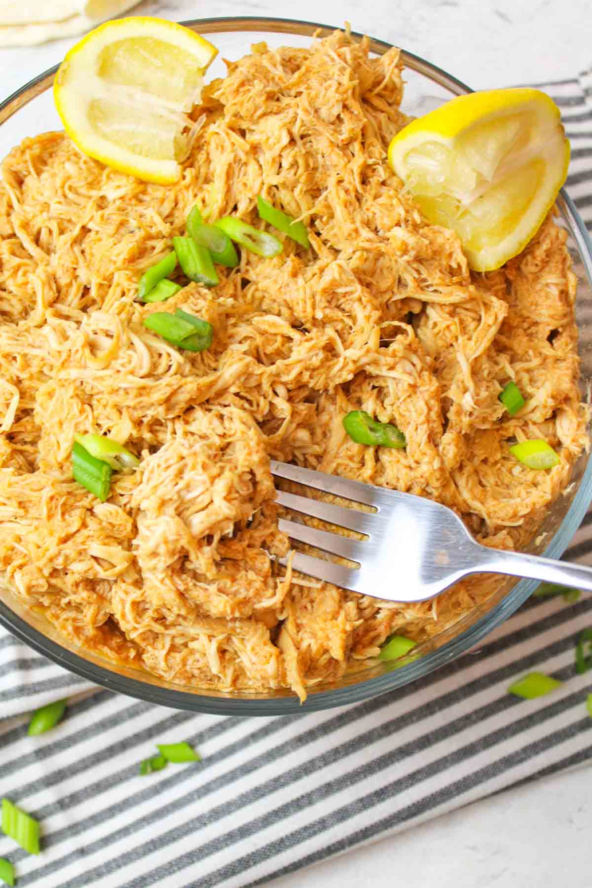a bowl filled with shredded enchilada chicken with a fork holding up a scoop of it
