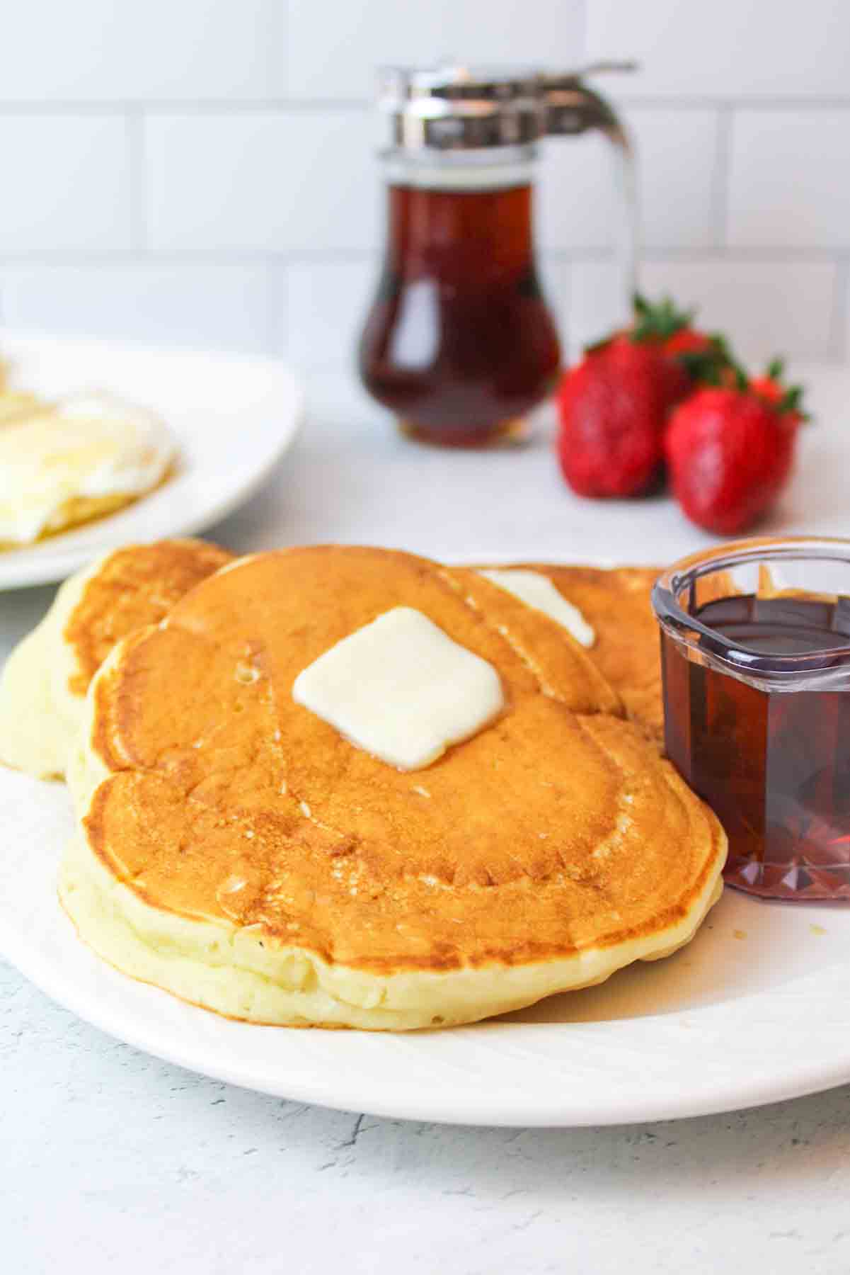 a close up of two golden pancakes on a plate with syrup and butter