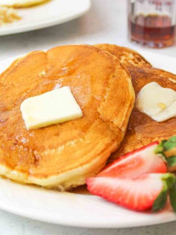 close up of golden buttermilk pancakes on a plate with butter and strawberries
