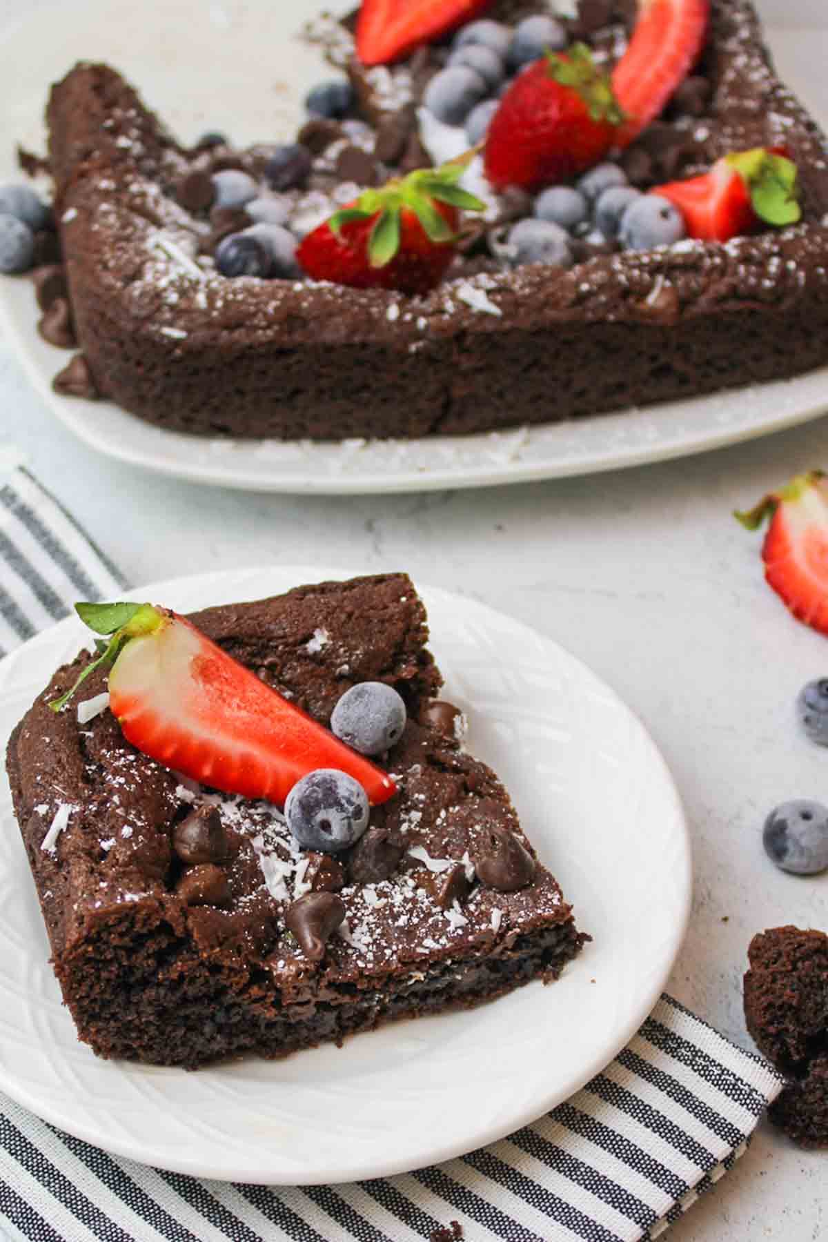 slcied Devils Food Cake Brownies on a white plate topped with fresh strawberries and blueberries