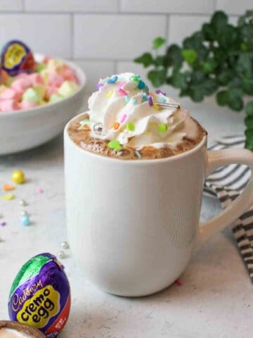 a mug filled with easter egg hot chocolate and topped with whipped cream and sprinkles.