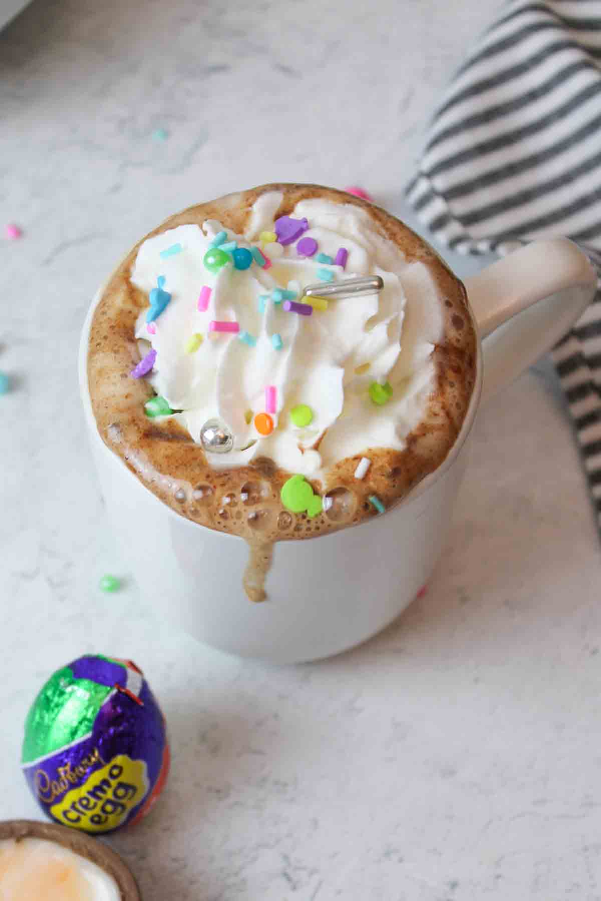 aerial view of a white mug filled with easter egg hot chocoalte and topped with whipped cream and sprinkles