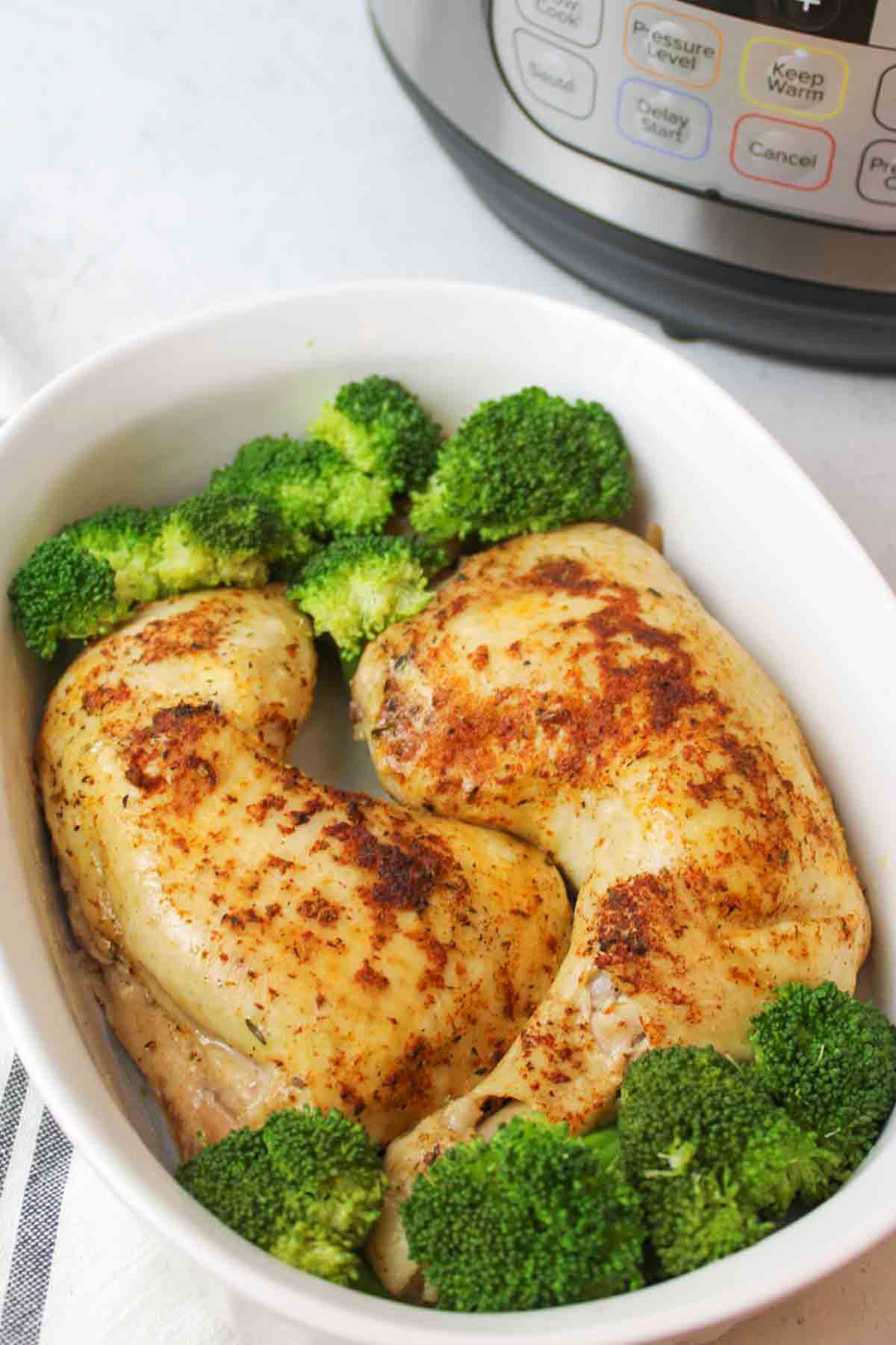 two cooked chicken quarters in a white dish with broccoli next to an instant pot