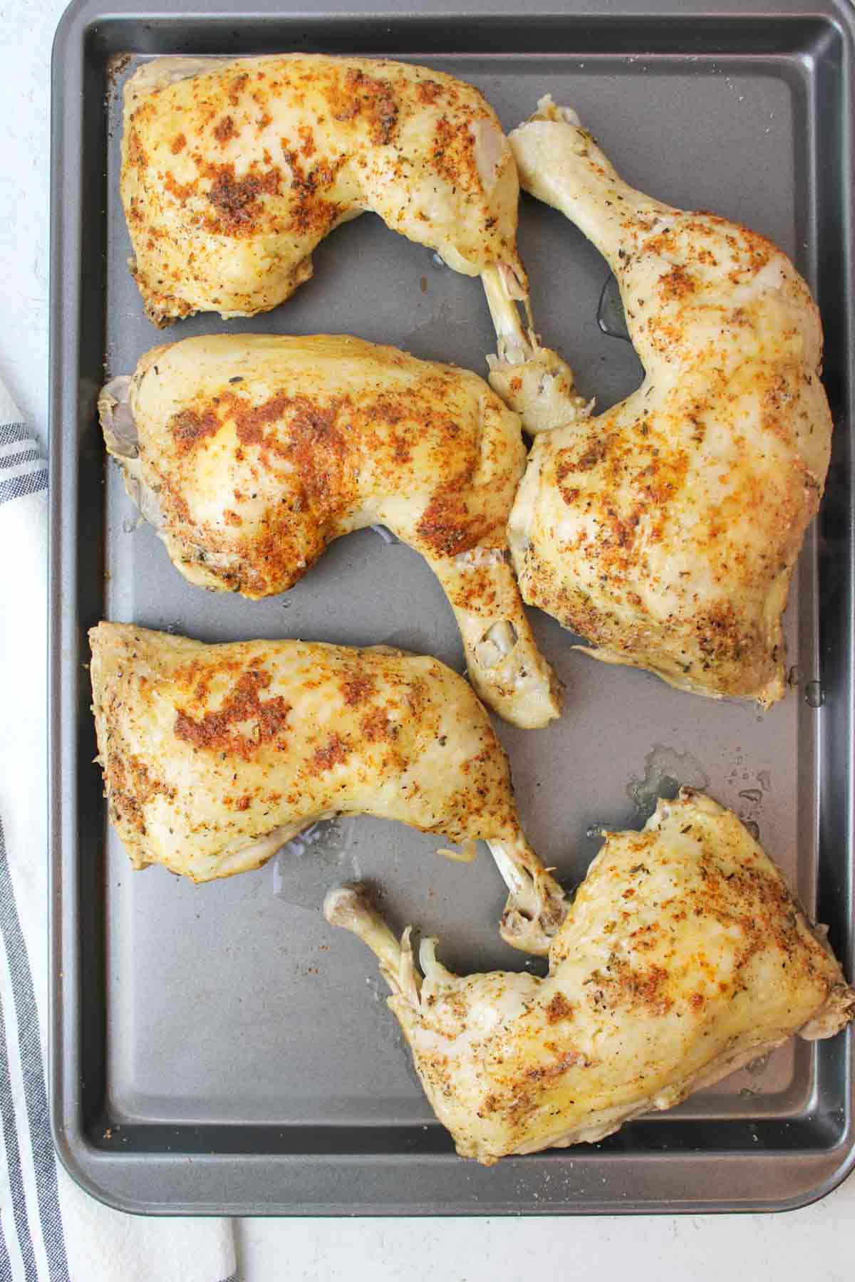 cooked chicken quarters on a baking sheet.