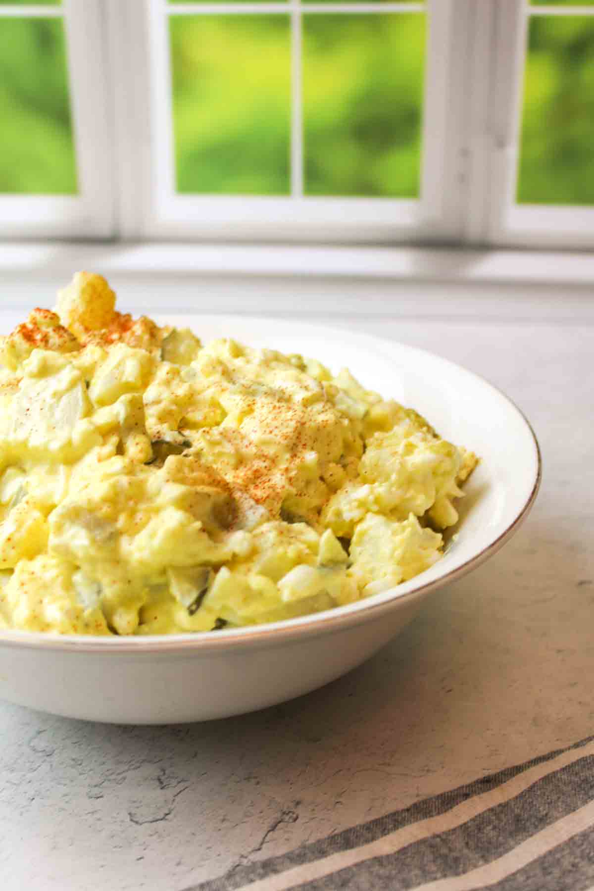 a white bowl of dill pickle potato salad in front of a window.