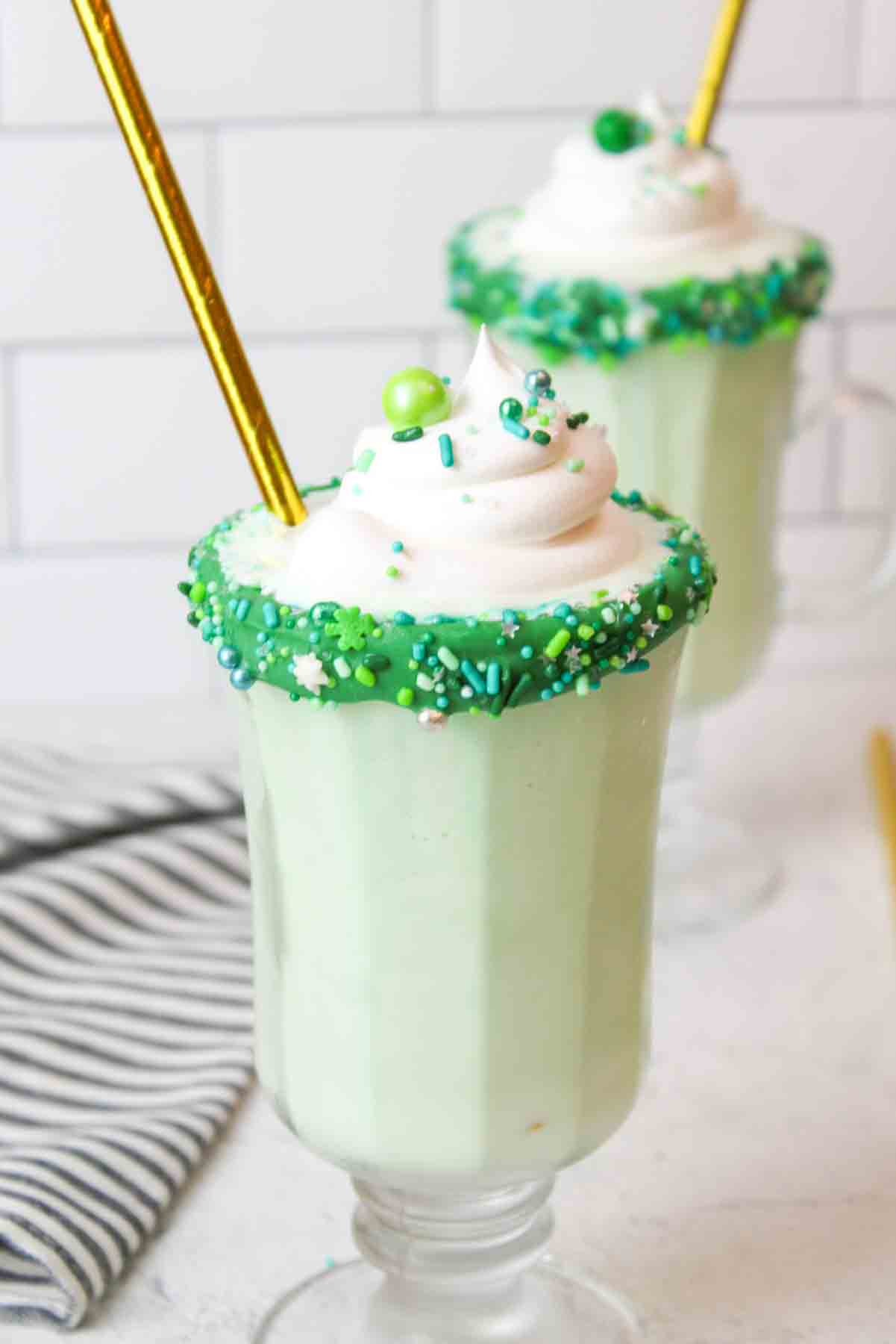 green mint shake in glass cups with gold straws, sprinkles, and whipped cream
