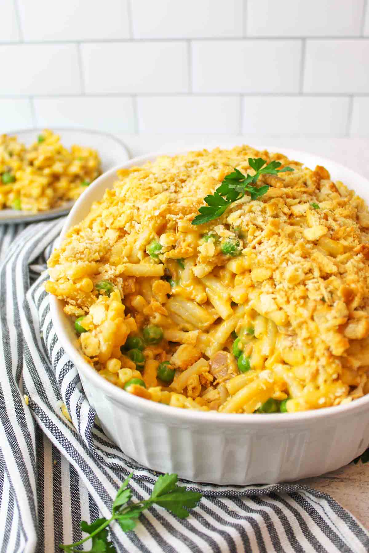 mac and cheese tuna casserole in a white oval dish with some missing and placed onto a plate in the background