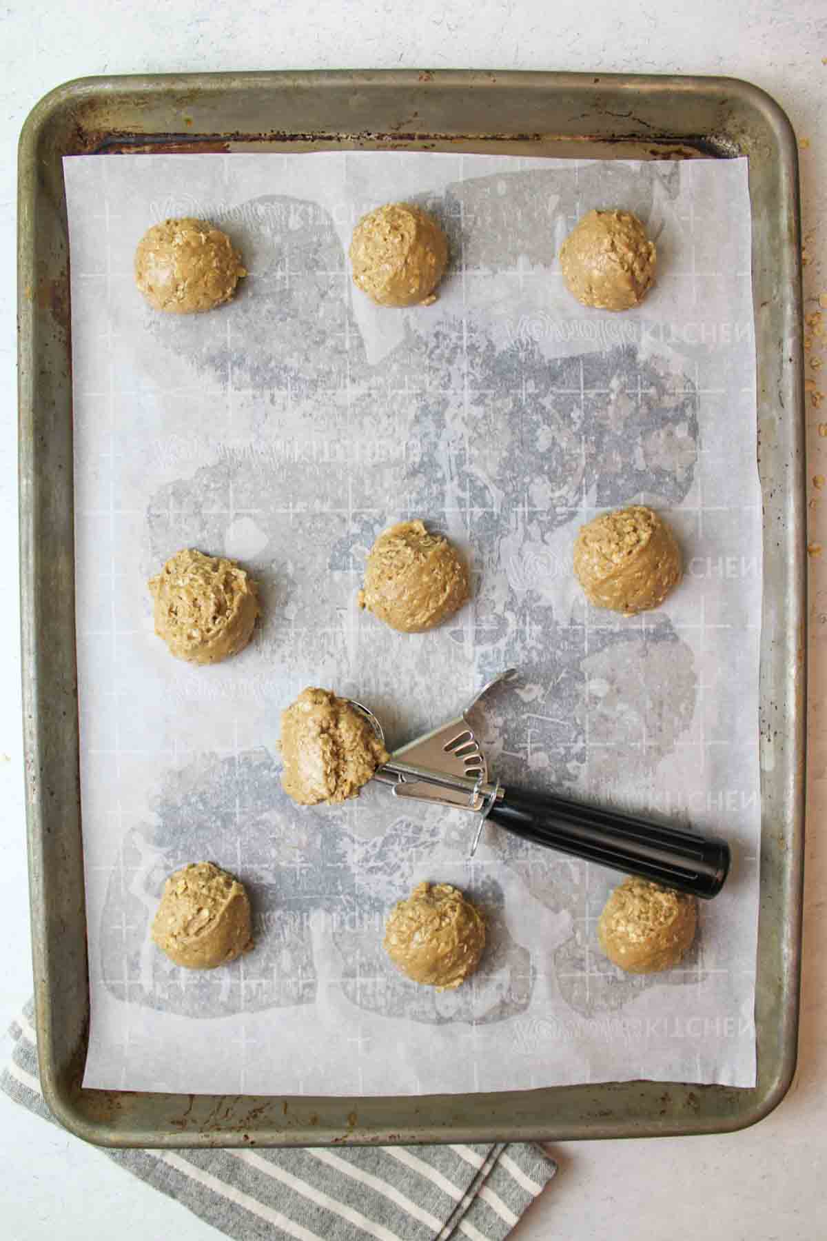 oatmeal cake mix cookie dough balls on baking sheet with a cookie scooper.