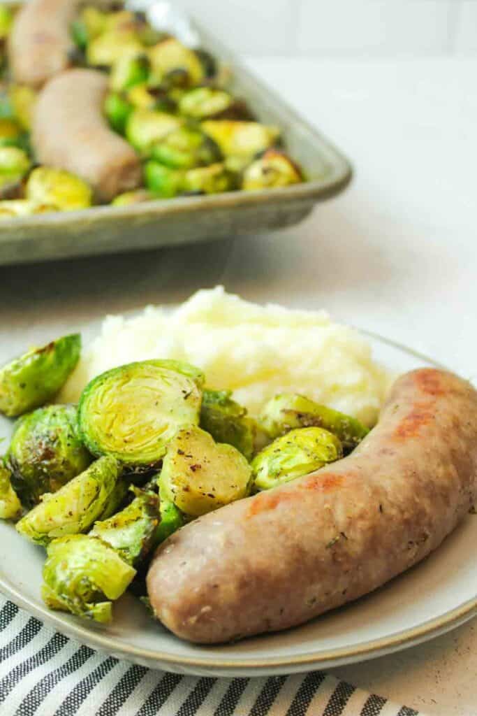 a cooked sausage next to some cooked brussel sprouts and mashed potatoes on a plate.
