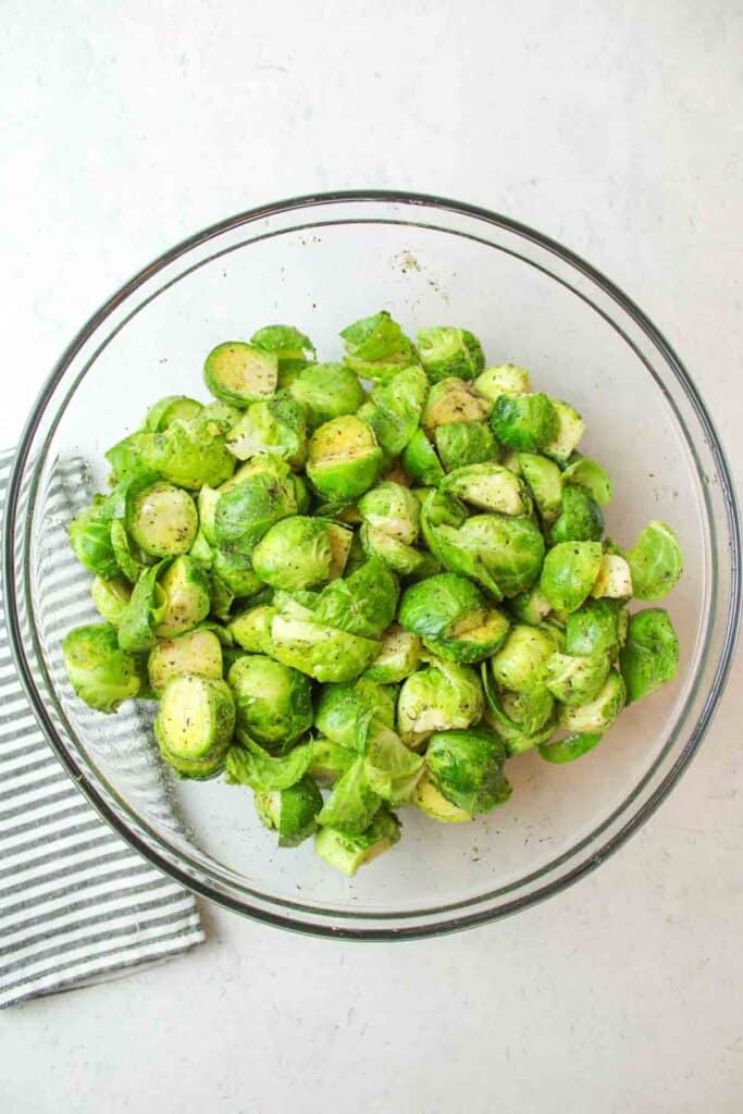 seasoned halved raw brussel sprouts in a glass bowl