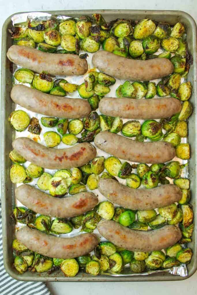 baked brussel sprouts and sausages on a baking sheet