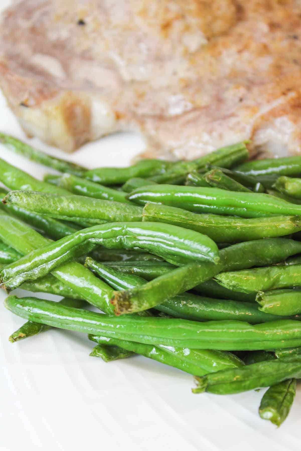 upclose view of cooked green beans with a pork chop in the background