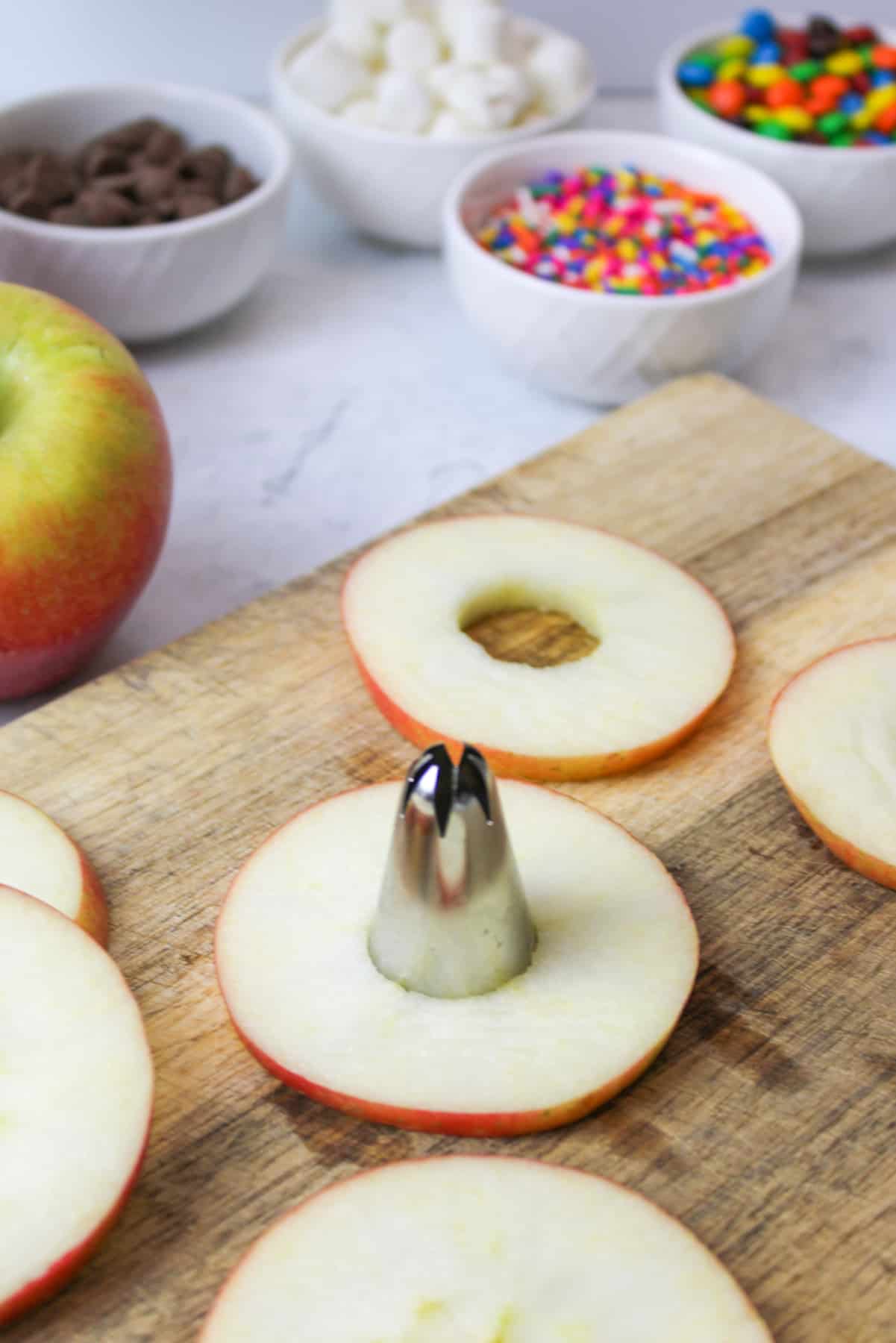 a frosting tip being used to cut out the center of a round apple slice.