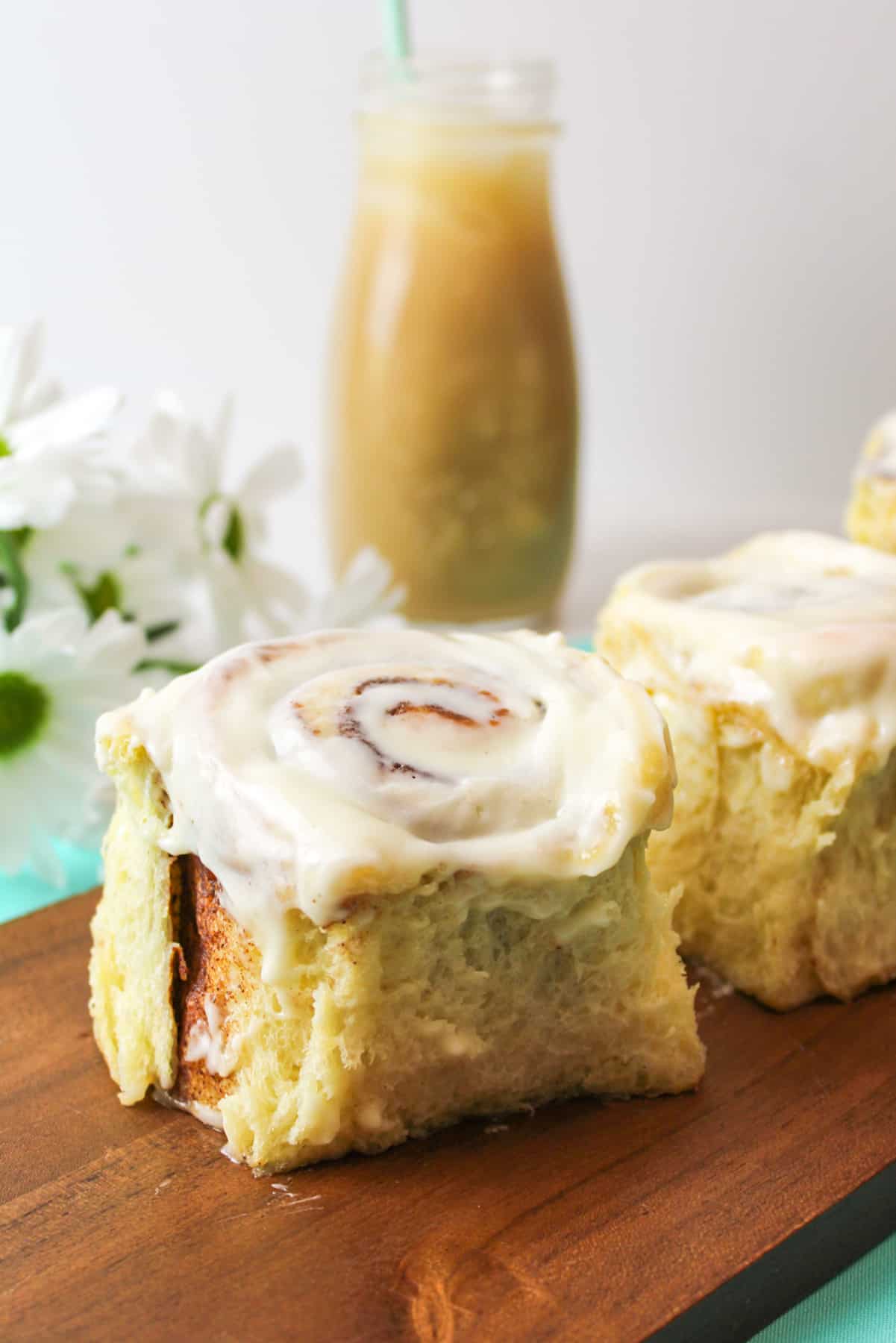 arranged cinnamon rolls on a wooden board with fresh flowers and bottle of coffee in background.