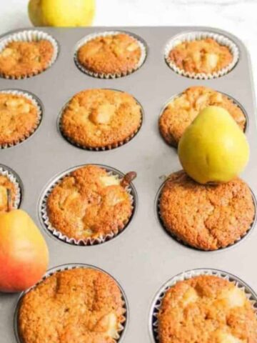 Pear Muffins in a muffin pan with fresh pears on top.
