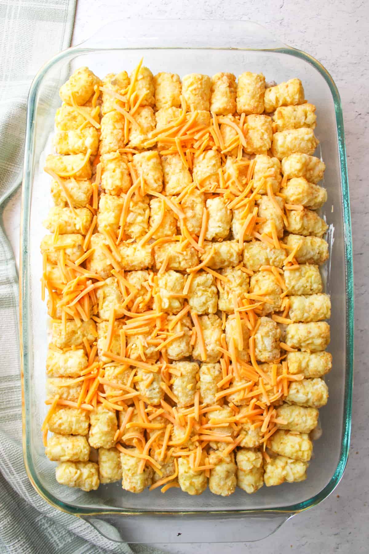 sprinkled cheese on top of tater tots in an unbaked tater tot casserole.