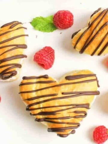 heart shaped cream puffs with chocolate drizzle and fresh raspberries around them.