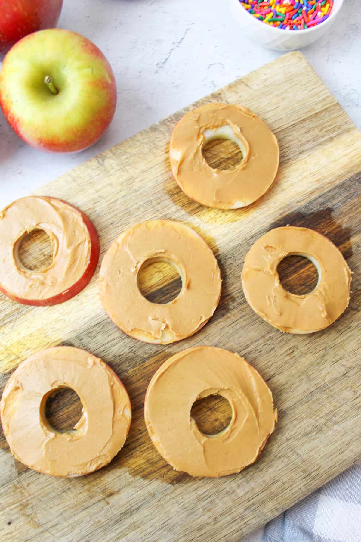apple rounds smothered in peanut butter on a wooden cutting board.