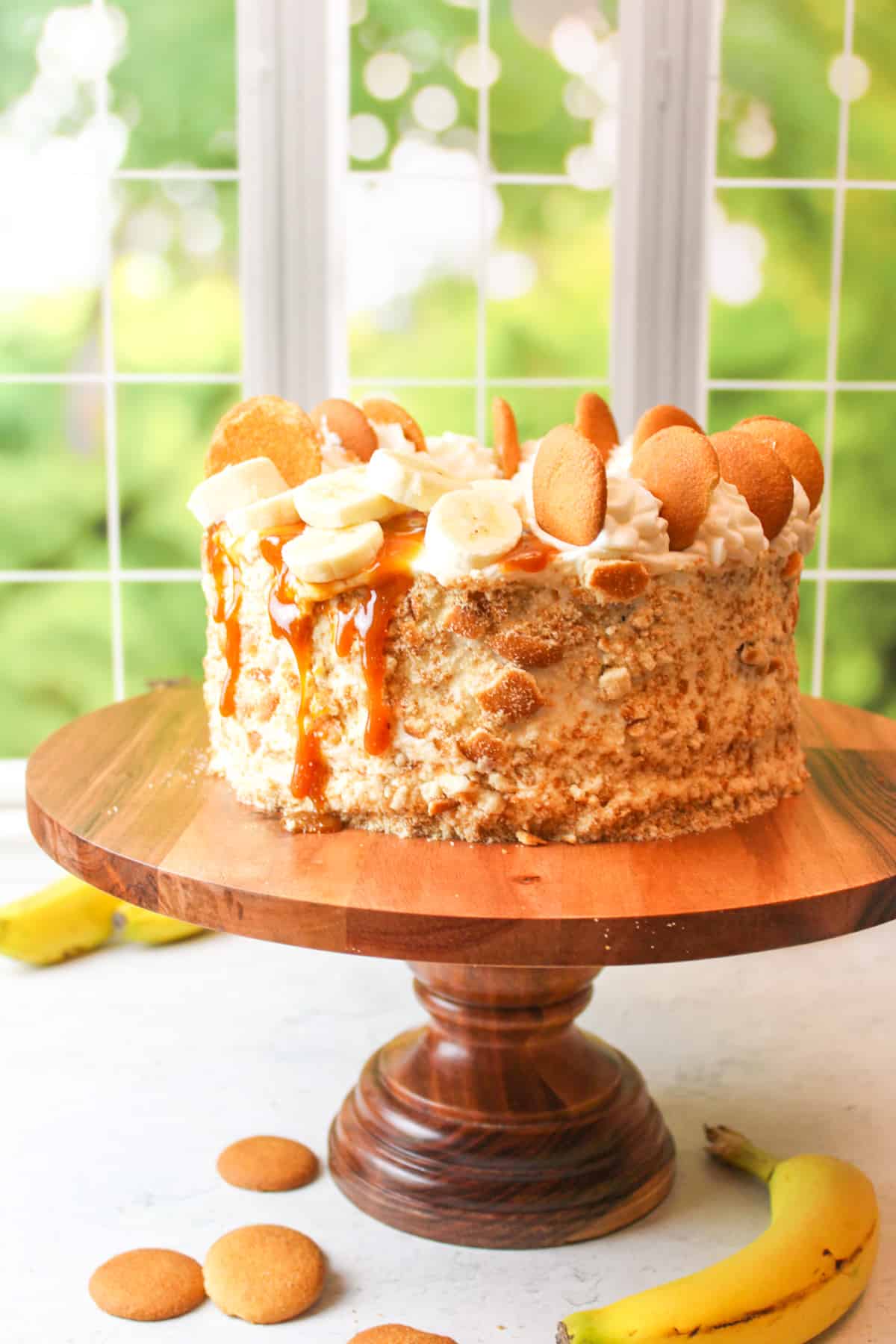 southern banana pudding cake fully decorated and sitting on a wooden cake stand.