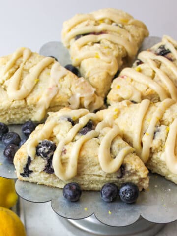 5 glazed blueberry scones on a metal stand with scattered fresh blueberries.