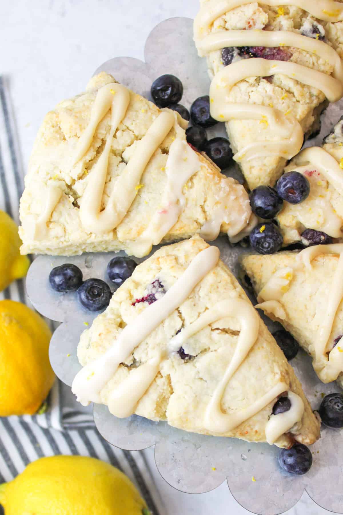 up close aerial view of glazed blueberry scones on a metal stand with fresh blueberries scattered around