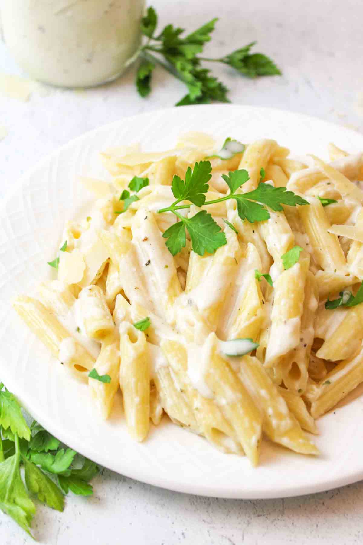 White plate with penne pasta, homemade cream cheese sauce, fresh parsley garnish.