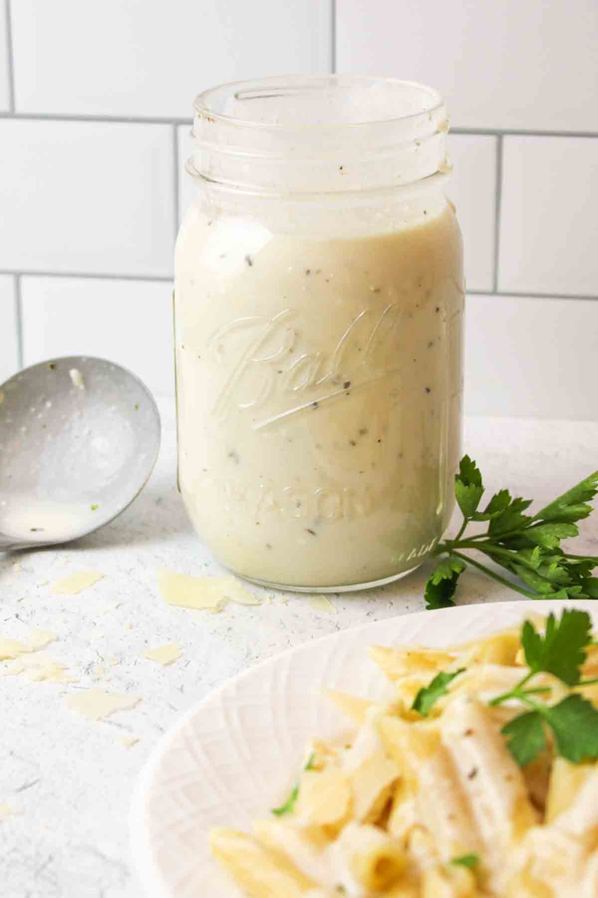 a jar of cream cheese alfredo next to fresh parsley.