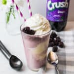 a close up view of a cup full of grape soda float with blackberries and whipped cream for garnish