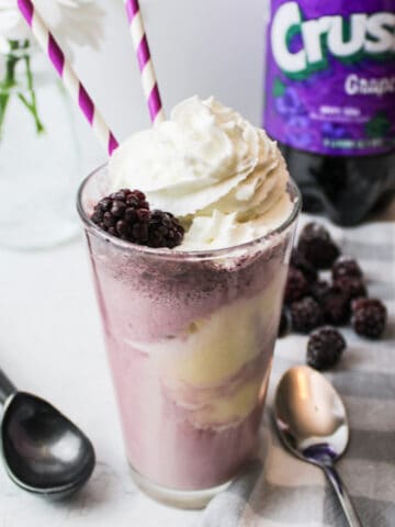 a cup full of grape soda float with blackberries and whipped cream for garnish.