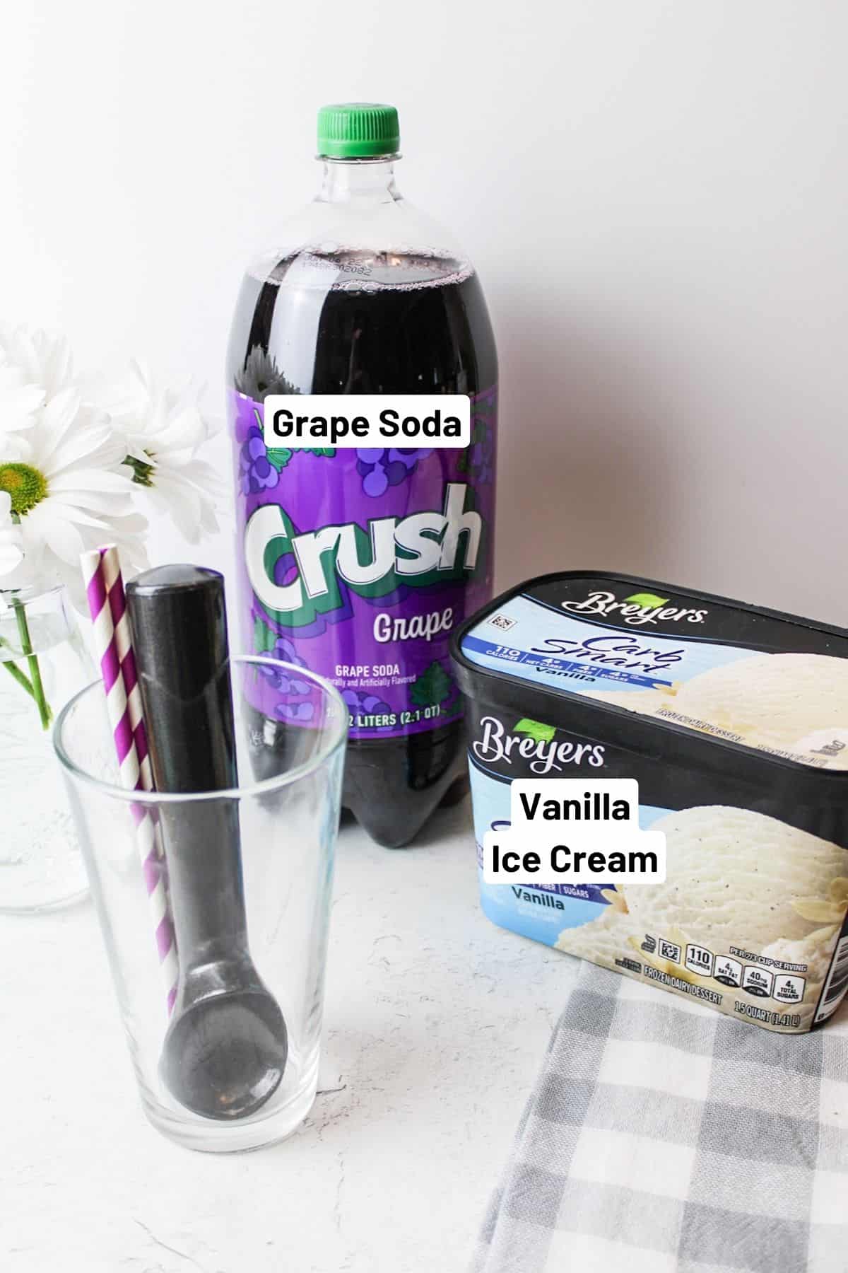 ingredients needed to make purple cow flaot plus a glass cup, ice cream scooper and straws next to fresh flowers