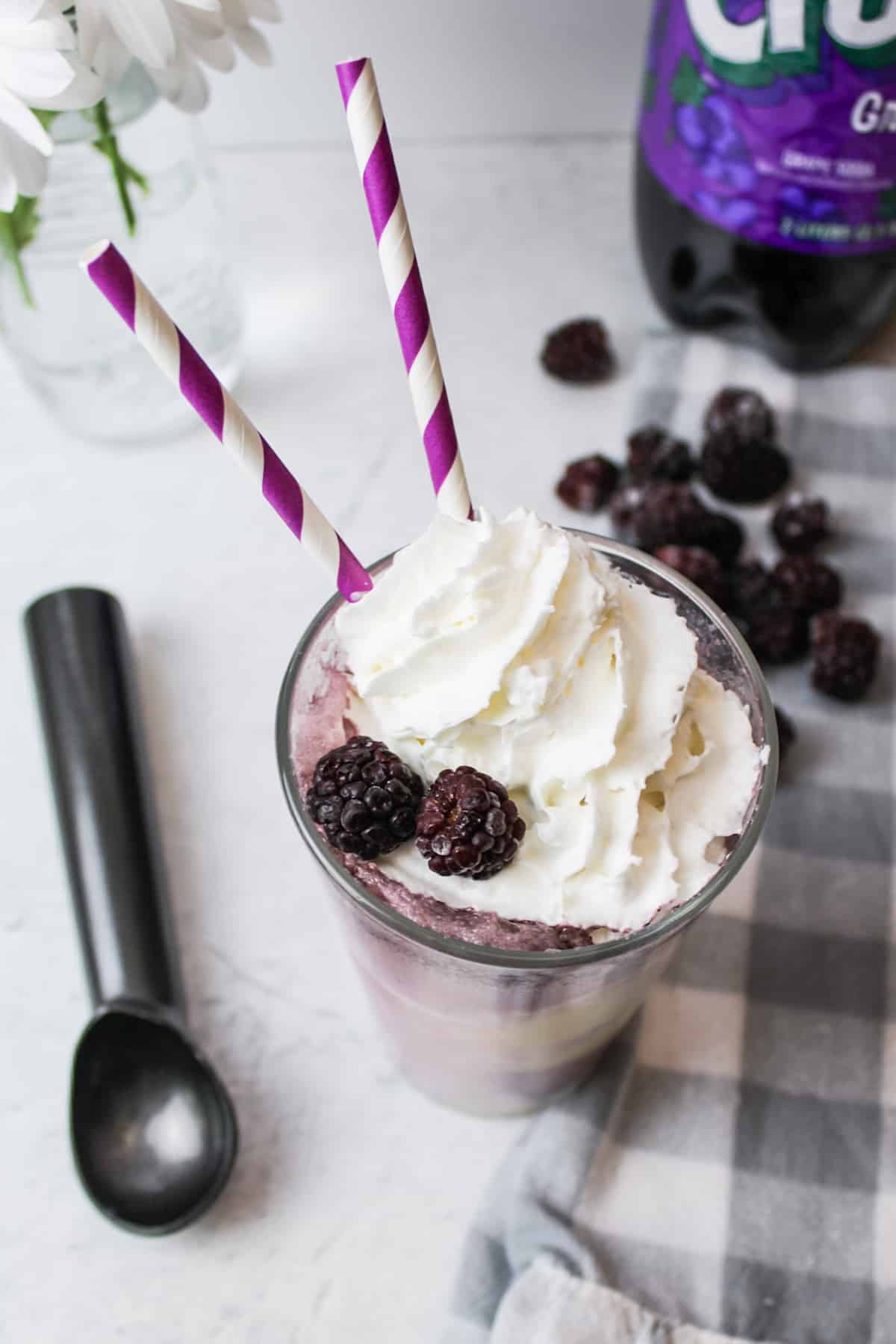 a purple cow float drink garnished with straws, whipped cream and blackberries.
