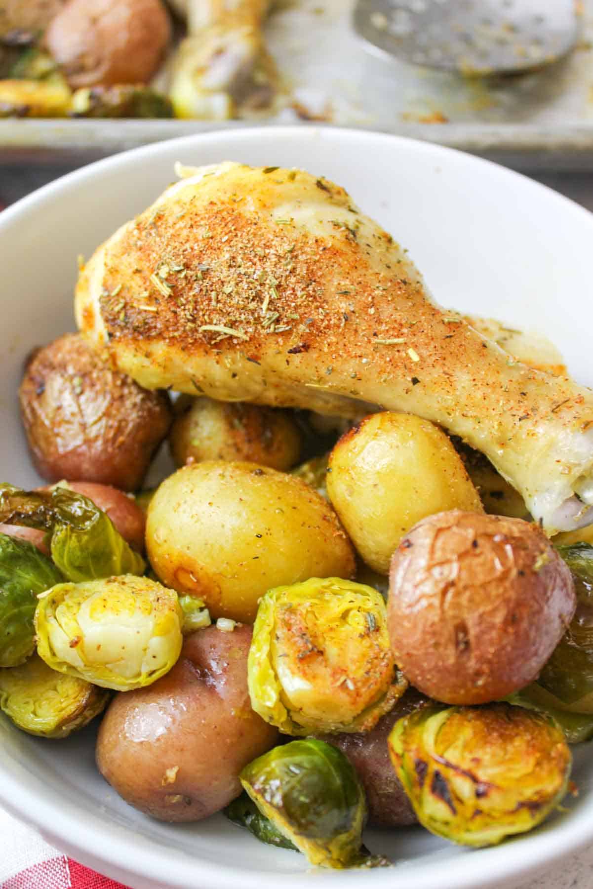 roasted baby potatoes, brussel sprouts and chicken legs in a bowl.